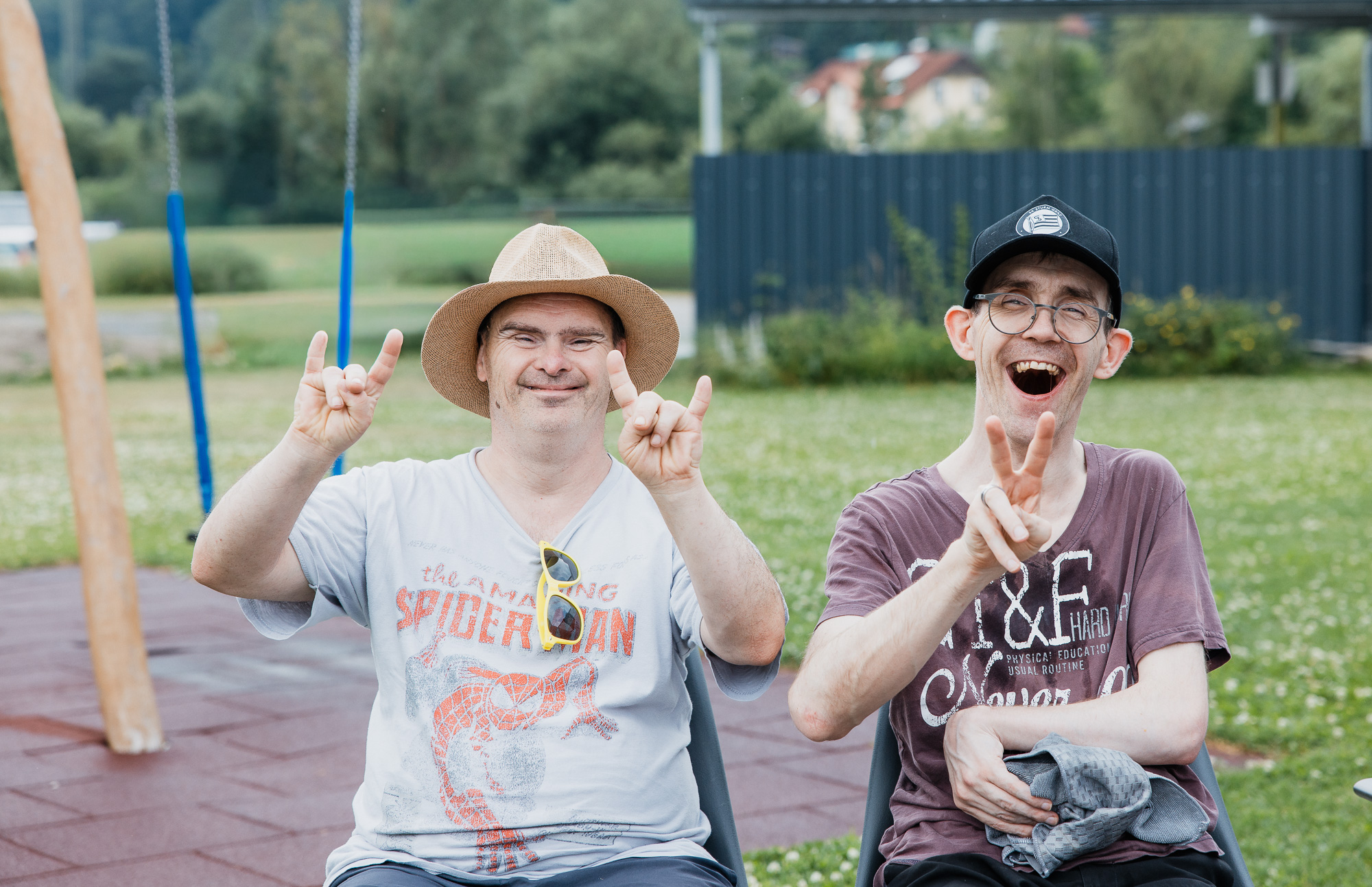 Zwei Männer sitzen lachend im Garten und grüßen mit Fingerzeichen Peace und Rockstar