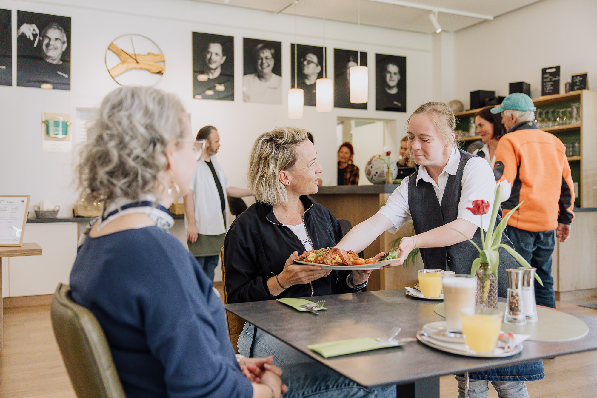 Eine Frau bedient zwei weitere Frauen im Restaurant und stellt gerade das bestellte Essen auf den Tisch