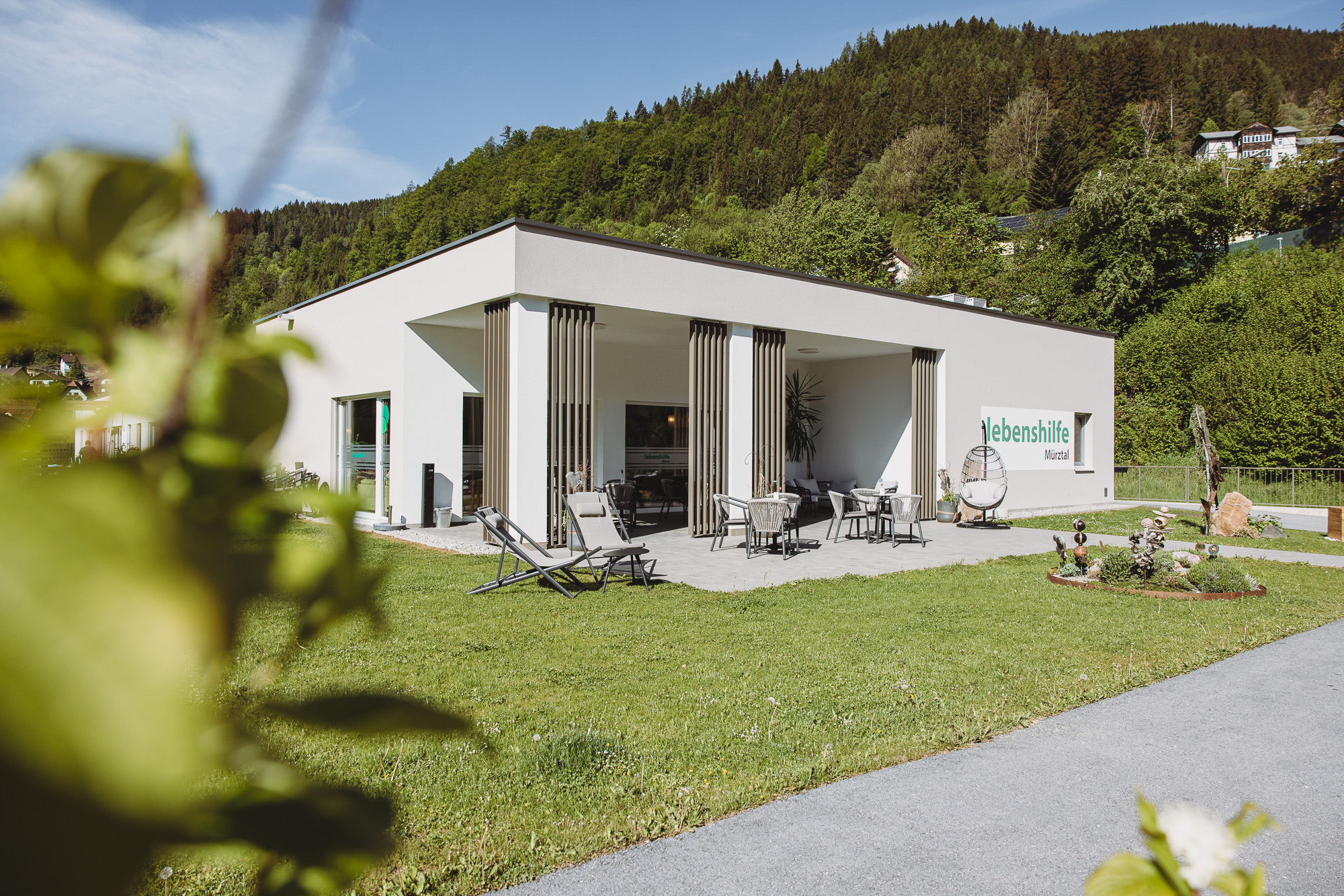 Ein Mann sitzt links auf einem gelben Sessel und spricht mit einer Frau, die auf einem grünen Sofa sitzt.